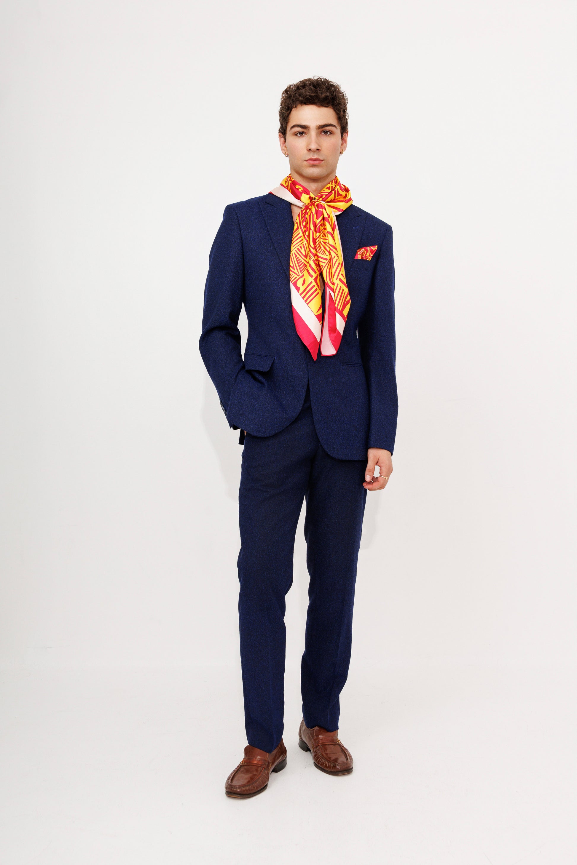 Male model in navy suit wearing orange Bana scarf as necktie